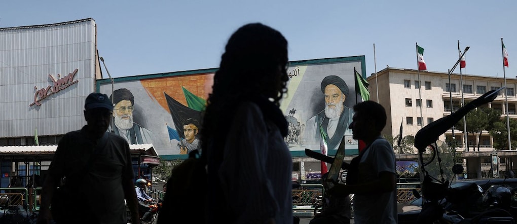 passanti a Teheran con sullo sfondo un poster dell’ Ayatollah Ruhollah Khomeini via REUTERS
