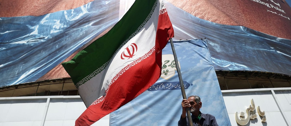 Un uomo tiene sventola una bandiera iraniana vicino a un cartellone pubblicitario anti-americano a Teheran via REUTERS