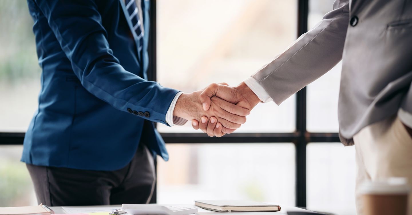 Two men shake hands in a business meeting. Scene is professional and formal. The handshake symbolizes agreement and trust between the two men Freedomz - stock.adobe.com