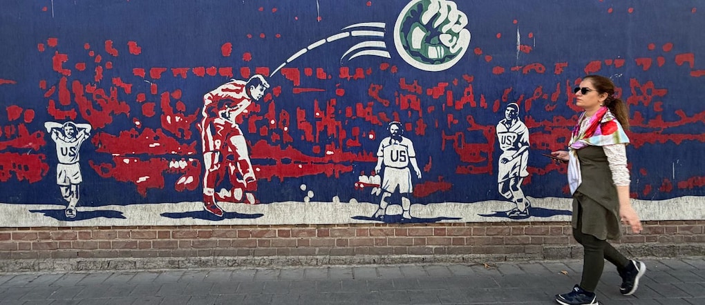 Una donna passa davanti a un murale che raffigura il centrocampista iraniano Hamid Estili mentre segna contro gli Stati Uniti durante la partita dei Mondiali FIFA del 1998, vinta dall’Iran per 2-1, sulla parete dell’ex ambasciata statunitense, ora trasformata in museo anti-americano, a Teheran, in Iran, venerdì 12 giugno 2026. (Foto AP/Vahid Salemi) APN
