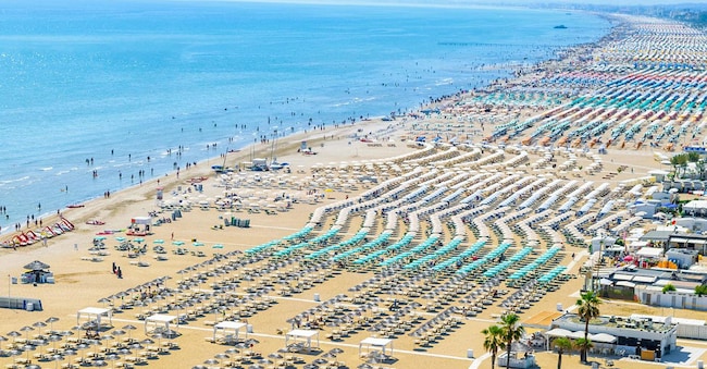 Vista aerea della spiaggia del resort di Rimini, in Italia, con numerosi ombrelloni e lettini durante il periodo estivo (Adobe Stock)