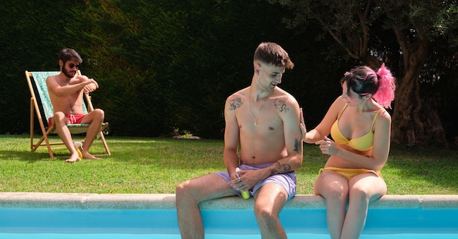 Tre giovani amici seduti sul bordo della piscina mentre si spalmano la crema solare. (Alamy Stock Photo)