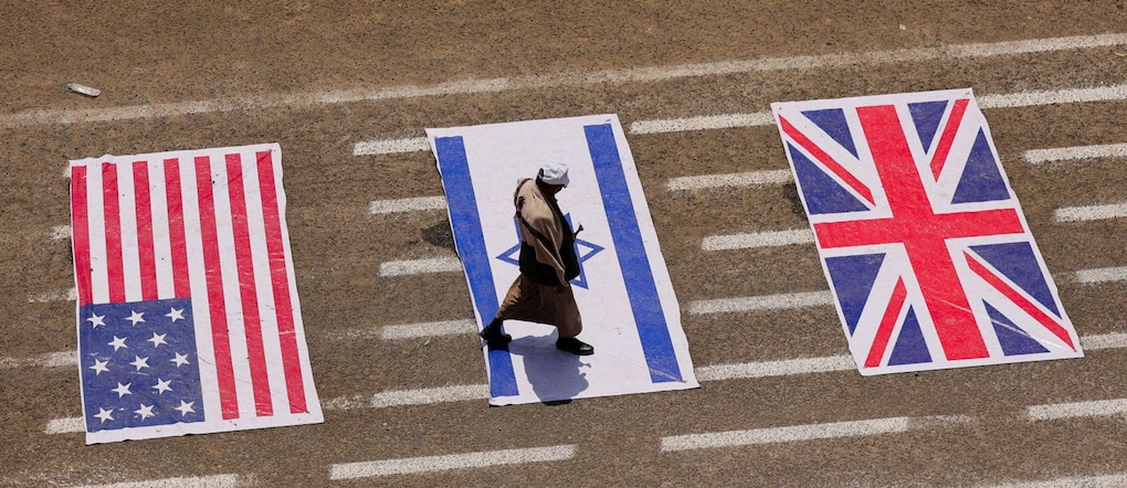 Un studente cammina sulle bandiere di Stati Uniti, Israele e Regno Unito durante una sfilata studentesca nel campus dell’Università di Sana’a REUTERS