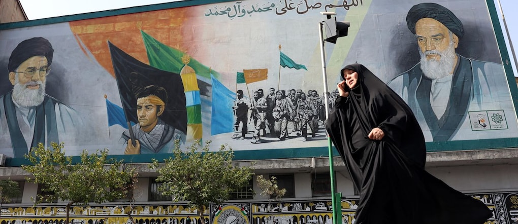 Una donna iraniana velata passa davanti a un murale raffigurante i defunti leader supremi iraniani.  EPA/ABEDIN TAHERKENAREH - EPA
