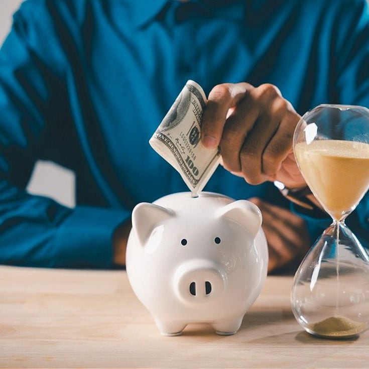 Hourglass money save cost company saving bank piggy business budget account time shows businessman putting hundred dollar bill into white ceramic piggy bank on wooden office desk.