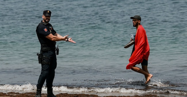 Un agente di polizia spagnolo fa un gesto mentre un migrante passa, a seguito dei recenti attraversamenti di massa di migranti a piedi e via mare dal Marocco verso il territorio spagnolo, a Ceuta, in Spagna, il 1° agosto 2026. REUTERS/Violeta Santos Moura REUTERS