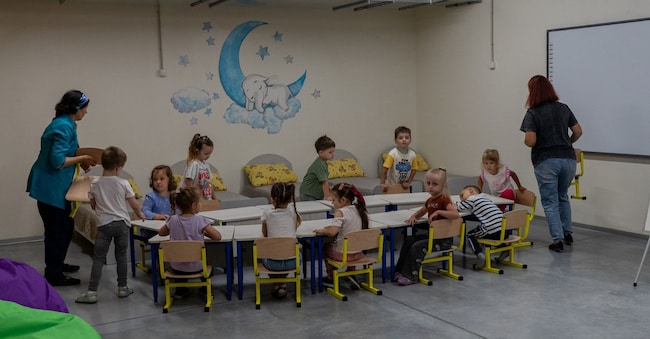 I bambini ascoltano la loro maestra nel primo asilo sotterraneo del Paese, costruito per proteggersi dai continui attacchi aerei russi, nel giorno dell'inaugurazione, nei pressi di Kharkiv, in Ucraina, martedì 21 luglio 2026. (AP Photo/Andrii Marienko)