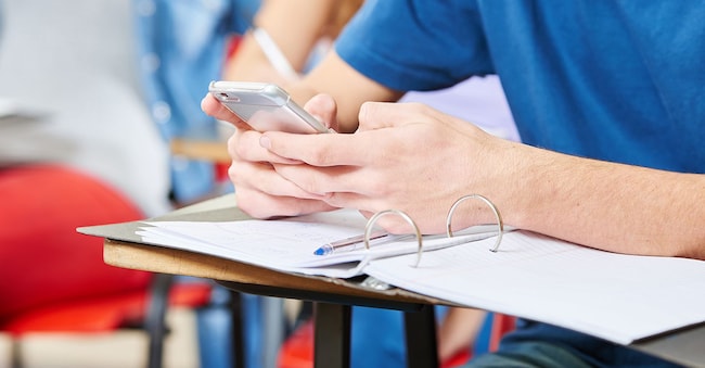 Uno studente legge un SMS sullo smartphone a scuola (Adobe Stock)