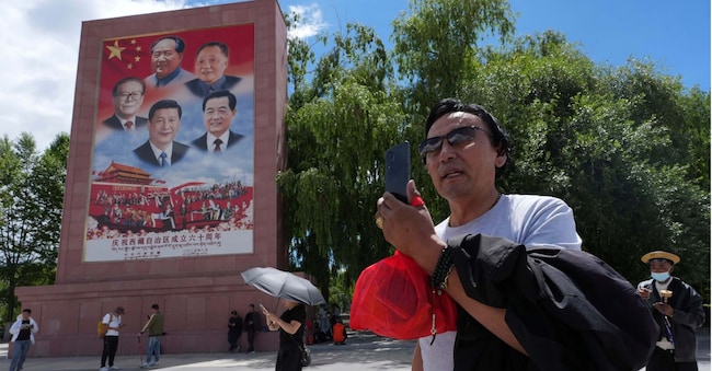 Un turista immortalato vicino a un manifesto che raffigura i leader cinesi, tra i quali primeggia Xi Jinping  APN
