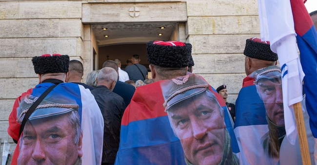 Uomini che indossano bandiere come mantelli, con l’effigie dell’ex generale serbo-bosniaco Ratko Mladic,  tra la folla radunata presso la chiesa di San Luca, in occasione dei funerali di stato (REUTERS)