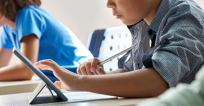Uno scolaro asiatico, dall'aria concentrata e diligente, che utilizza un tablet mentre è seduto in classe insieme a un gruppo di compagni.  (Adobe Stock)