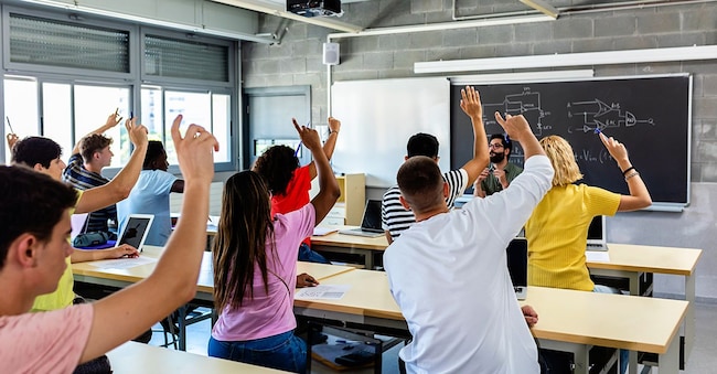 Gruppo di studenti delle scuole superiori che alzano la mano in classe, durante la lezione. (Adobe Stock)