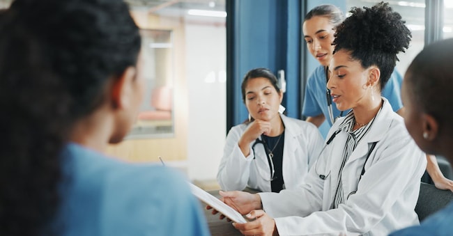 Doctors, nurse and women on clipboard in meeting, collaboration or teamwork for hospital planning, medical or life insurance. Talking, leadership and healthcare workers on paper in diversity research. SneakyPeakPoints/peopleimages.com - stock.adobe.com