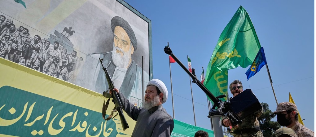 Un religioso sciita armato passa a bordo di un veicolo militare davanti a un cartellone pubblicitario raffigurante l’ayatollah Ruhollah Khomeini, fondatore della Repubblica islamica, durante la parata in stile militare “Janfada”, o “Sacrificio per l’Iran”, organizzata dallo Sato a Teheran (AP Photo/Vahid Salemi) APN
