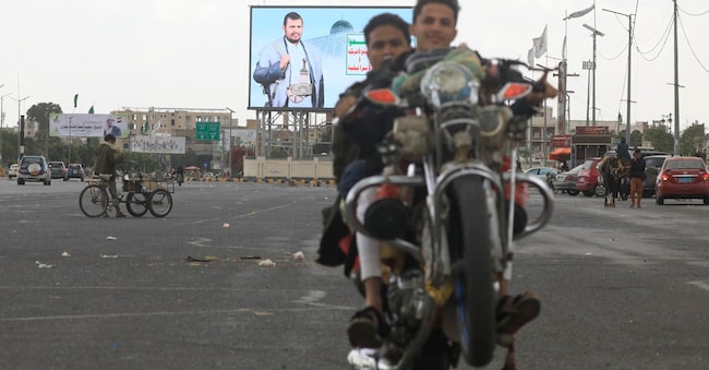 Alle spalle dei due motociclisti una pubblicità digitale raffigurante il leader degli  Houthi Abdul-Malik al-Houthi, lungo una strada di Sana'a nello Yemen EPA