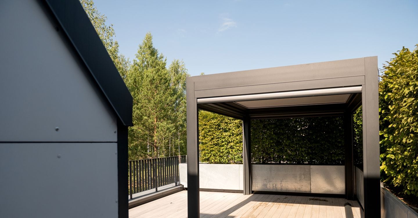 A sleek pergola on a wooden deck, surrounded by trees and clear skies