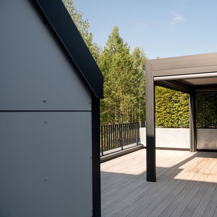 A sleek pergola on a wooden deck, surrounded by trees and clear skies