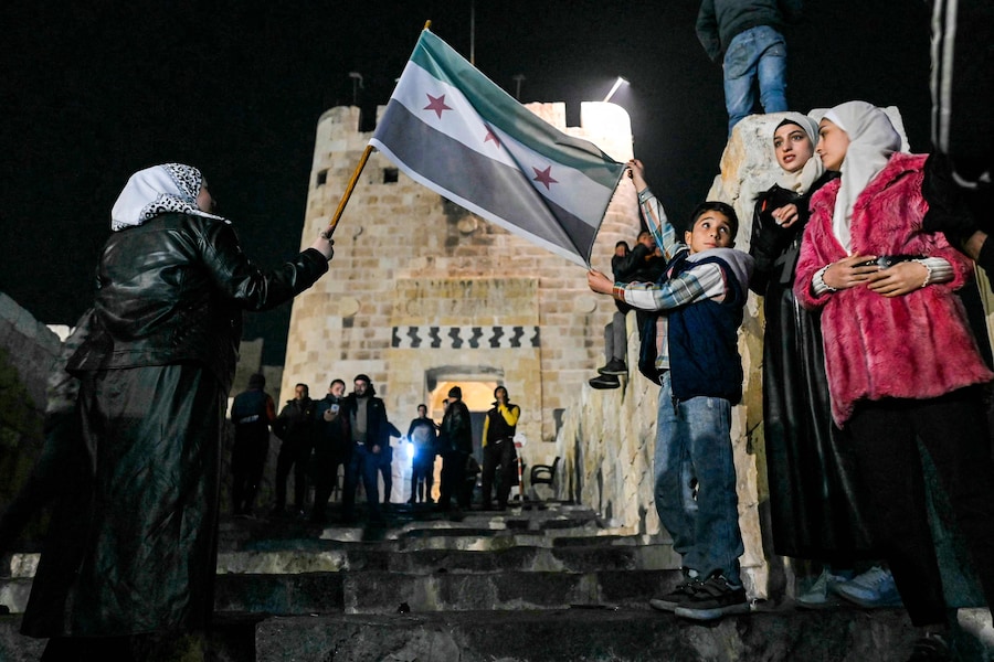 Un ragazzo dispiega una bandiera dell’opposizione siriana tenuta da una donna fuori dalla Cittadella di Aleppo, nel nord della Siria, il 10 dicembre 2024. I ribelli guidati dagli islamisti hanno preso la capitale siriana Damasco in un’offensiva lampo l’8 dicembre, estromettendo il presidente Bashar al-Assad e ponendo fine a cinque decenni di governo Baath nel paese (AFP)