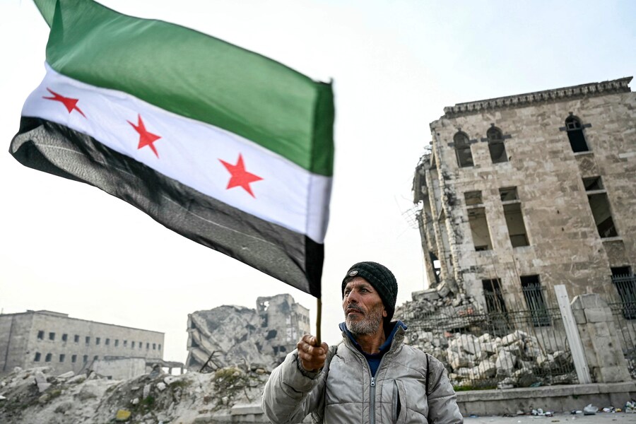 Un uomo sventola una bandiera dell’opposizione siriana nella Cittadella di Aleppo, nel nord della Siria, l’11 dicembre 2024. L’8 dicembre, i ribelli guidati dagli islamisti hanno preso la capitale siriana Damasco con un’offensiva lampo, rovesciando il presidente Bashar al-Assad e ponendo fine a cinque decenni di governo Baath nel paese (AFP)