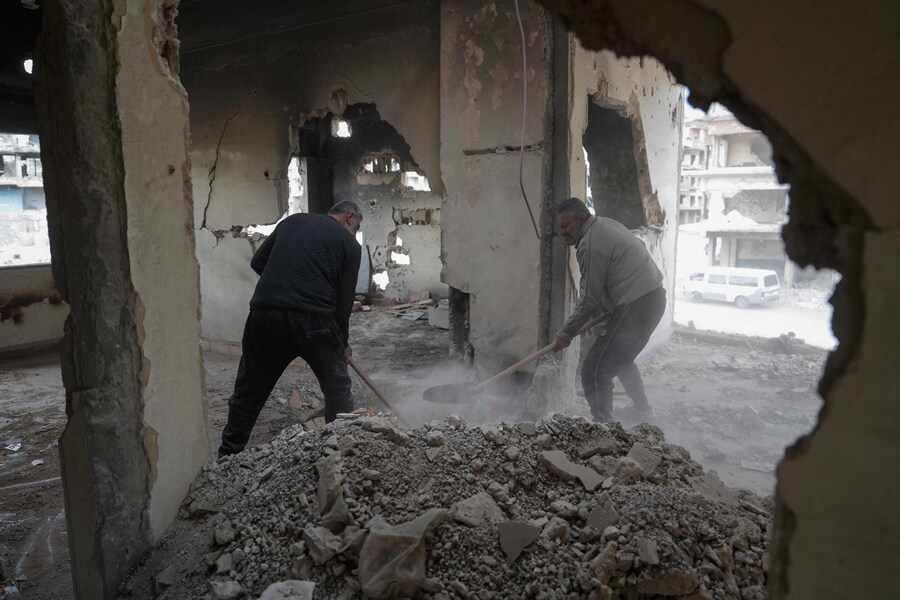 Persone rimuovono macerie e detriti dalle loro case nel campo di Yarmuk. (MUHAMMAD HAJ KADOUR / AFP)