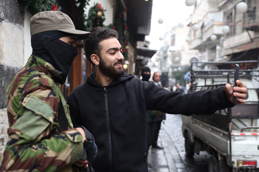 Un uomo siriano scatta un selfie con un membro delle forze di sicurezza (OMAR HAJ KADOUR / AFP)