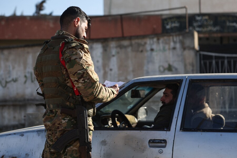 Un membro delle forze di sicurezza del governo provvisorio siriano controlla l’identificazione di un automobilista a un posto di blocco a Homs. (OMAR HAJ KADOUR / AFP)
