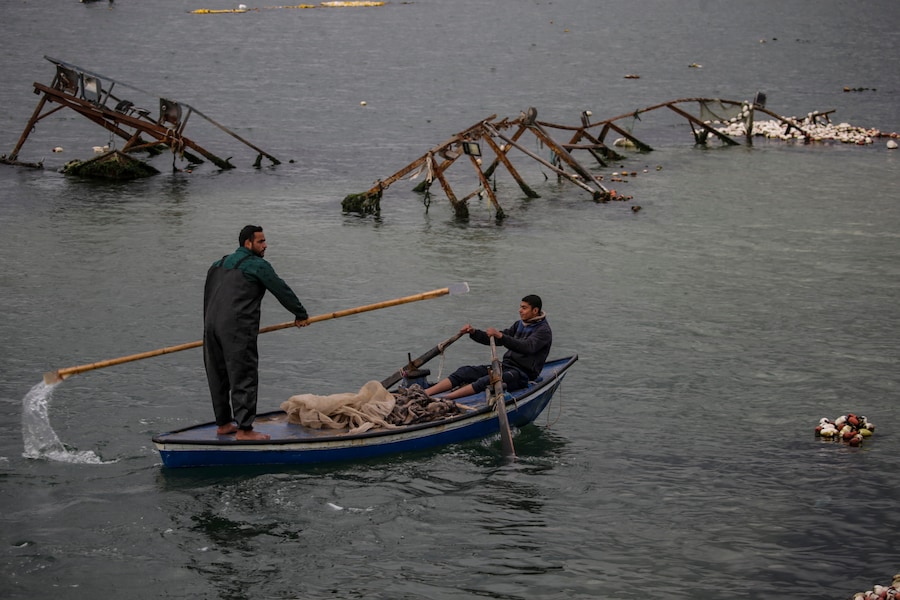 Persone su una piccola barca a remi guardano in acqua vicino alle navi distrutte dei pescatori palestinesi che galleggiano sulla superficie dell’acqua durante il conflitto nel porto di Gaza distrutto durante il cessate il fuoco tra Israele e Hamas, a Gaza City. (EPA)