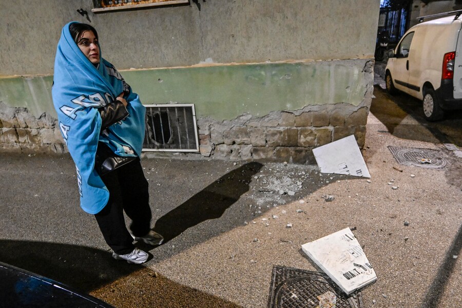 Una donna ricoperta con una coperta di pile del Napoli cammina tra i calcinacci caduti in strada nel quartiere Bagnoli dopo le scosse di terremoto nella notte, Napoli, 13 marzo 2025. ANSA / CIRO FUSCO (CIRO FUSCO)