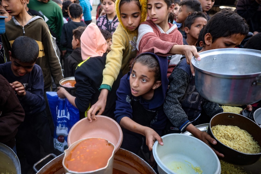 Bambini palestinesi ricevono il pasto di digiuno iftar per la loro famiglia in un punto di distribuzione di cibo gratuito nel campo profughi di Nuseirat, nella Striscia di Gaza centrale, durante il mese di digiuno musulmano del Ramadan. (AFP)