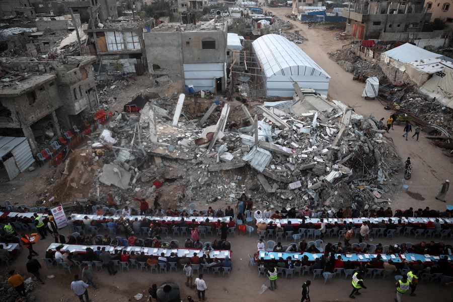 Questa fotografia aerea mostra i palestinesi riuniti per un pasto comune per la rottura del digiuno iftar, tra le devastazioni del campo profughi di Nuseirat, nella Striscia di Gaza centrale, durante il mese sacro di digiuno musulmano del Ramadan. (AFP)