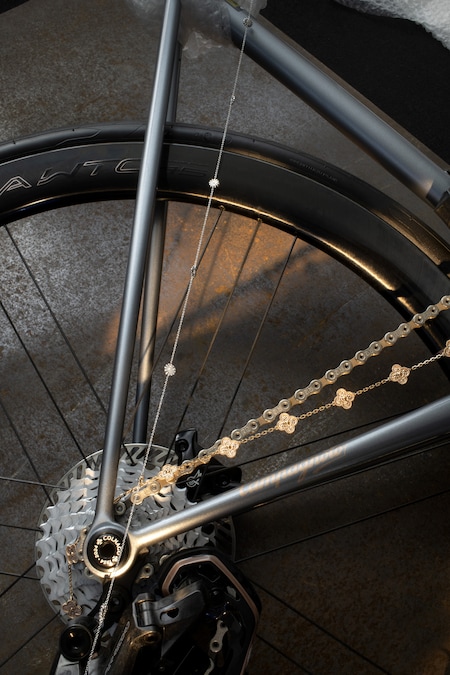 Dall’alto, collana in oro bianco e diamanti, collezione Margherita, DAMIANI (8.490 €). Sautoir Vintage Alhambra in oro rosa, VAN CLEEF & ARPELS (20.000 €). Sullo sfondo, dettaglio della bicicletta da corsa Steelnovo, in acciaio e componentistica Campagnolo, COLNAGO (17.500 €, in edizione limitata di 70 esemplari).