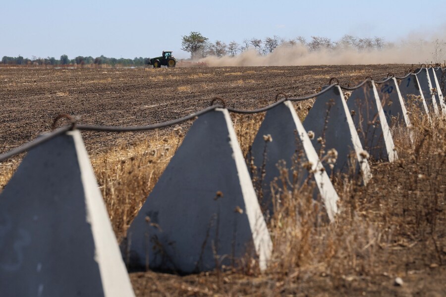 Un lavoratore agricolo aziona un trattore vicino alle fortificazioni anticarro, chiamate "denti di drago", durante l'attacco russo all'Ucraina, nella regione di Kherson, in Ucraina. (REUTERS/Ivan Antypenko)