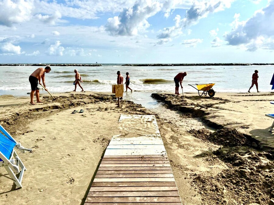 Alcuni bagnanti intervengono per riportare alla normalità una spiaggia di Igea Marina danneggiata dal temporale che si è abbattuto prima dell'alba sulla riviera romagnola. Igea Marina, 24 agosto 2025 (ANSA)