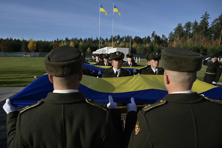 I militari della Guardia d’Onore tengono una bandiera ucraina sopra le bare di soldati ucraini non identificati durante una cerimonia funebre al Cimitero Nazionale Militare Memoriale vicino a Kiev (AFP)