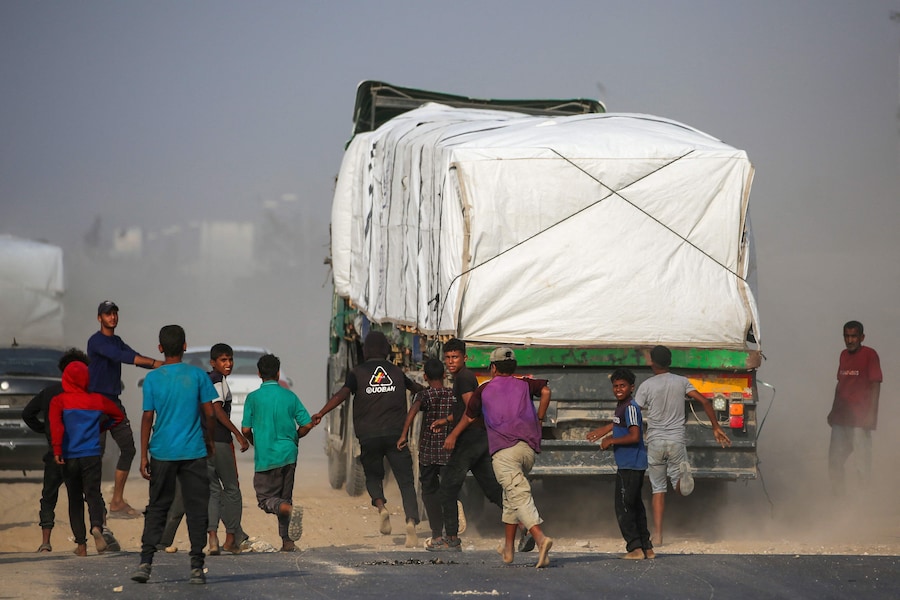Palestinesi sfollati inseguono i camion che percorrono la strada di Salah al-Din nella Striscia di Gaza centrale, vicino a Deir al-Balah, mentre cercano di ottenere aiuti umanitari il 9 novembre 2025. (Foto di Eyad Baba / AFP) (AFP)