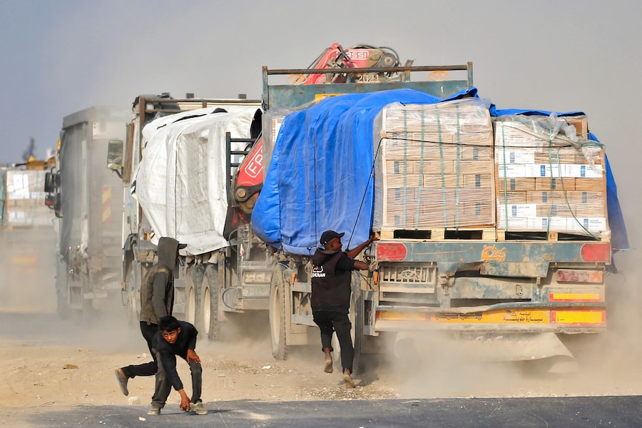 Uno sfollato palestinese tenta di salire su un camion che viaggia lungo la strada di Salah al-Din nella Striscia di Gaza centrale, vicino a Deir al-Balah, mentre la gente cerca di ottenere aiuti umanitari il 9 novembre 2025. (Foto di Eyad Baba / AFP) (AFP)