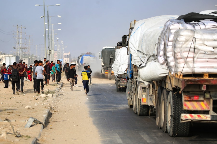 Palestinesi sfollati inseguono i camion che percorrono la strada di Salah al-Din nella Striscia di Gaza centrale, vicino a Deir al-Balah, mentre cercano di ottenere aiuti umanitari il 9 novembre 2025. (Foto di Eyad Baba / AFP) (AFP)