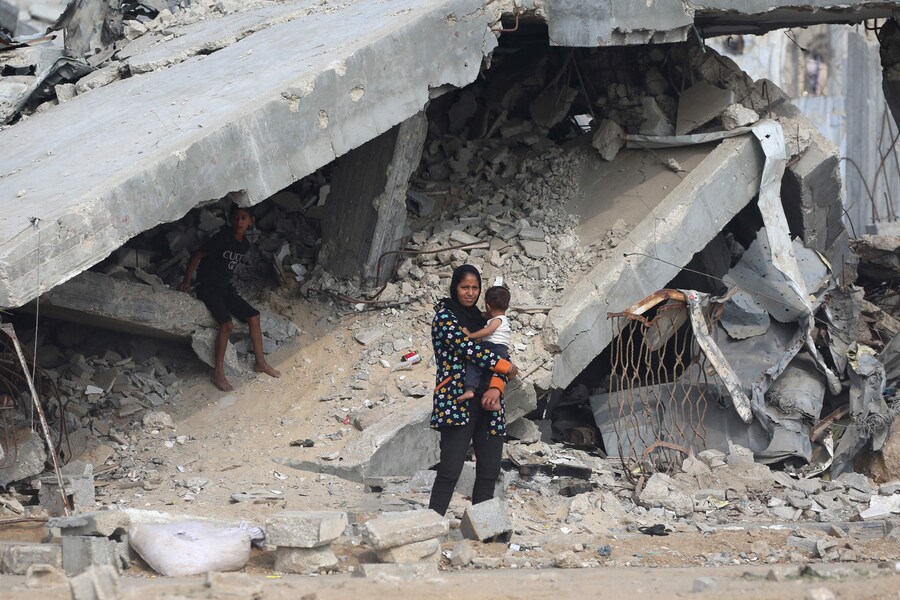 Una donna palestinese porta il suo bambino davanti a edifici distrutti lungo una strada vicino al campo profughi di Nuseirat, nel centro della Striscia di Gaza, il 9 novembre 2025, dopo la tregua promossa dagli Stati Uniti che ha fermato la guerra di due anni. La prima fase dell'accordo per il cessate il fuoco a Gaza, mediato il mese scorso dal Presidente degli Stati Uniti, ha aperto la strada allo scambio di ostaggi israeliani e prigionieri palestinesi. (Foto di Eyad Baba / AFP) (AFP)