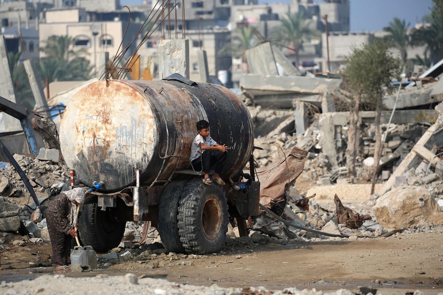 Una donna palestinese raccoglie acqua mentre un bambino si siede sulla cisterna lungo una strada vicino al campo profughi di Nuseirat, nella Striscia di Gaza centrale, il 9 novembre 2025, dopo la tregua promossa dagli Stati Uniti che ha fermato la guerra di due anni. La prima fase dell'accordo per il cessate il fuoco a Gaza, mediato il mese scorso dal Presidente degli Stati Uniti, ha aperto la strada allo scambio di ostaggi israeliani e prigionieri palestinesi. (Foto di Eyad Baba / AFP) (AFP)