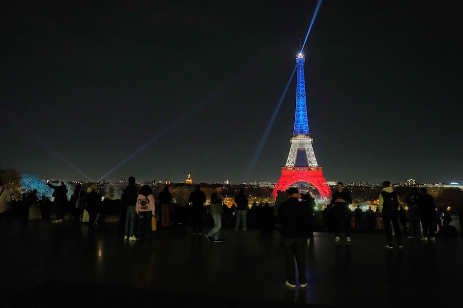 La gente si raduna in Plaza del Trocadero mentre la Torre Eiffel è illuminata con i colori della bandiera nazionale francese a Parigi, per onorare le vittime degli attacchi terroristici alla sala concerti Bataclan, ai caffè e allo stadio nazionale 10 anni fa (APN)