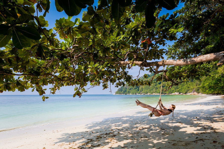 Giovane turista si rilassa su un’altalena su una spiaggia segreta dell’isola di Pangkor, in Malesia. Splendido paesaggio marino e porto ripreso nel sud-est asiatico.