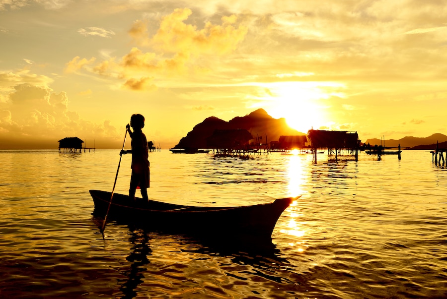 Silhouette di un bambino che sguazza su una barca vicino al villaggio di Bajau Laut nell’isola di Maiga a Semporna, Sabah Borneo, Malesia.