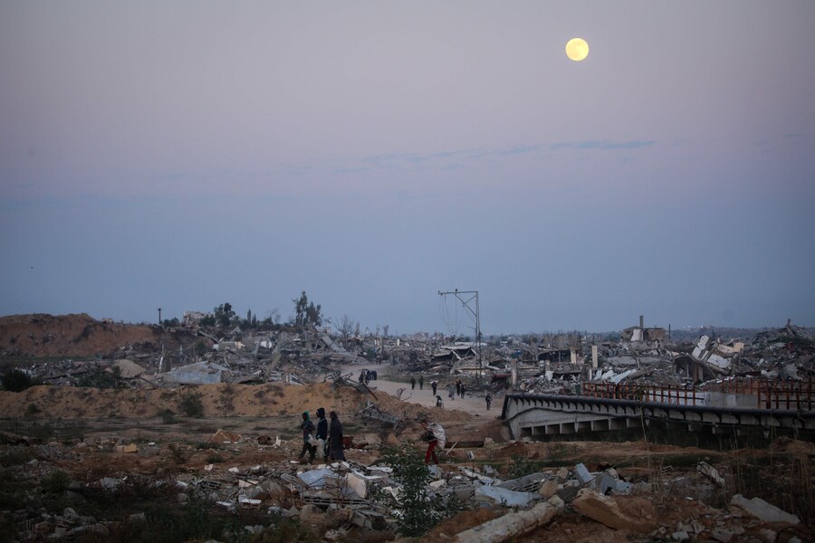 Persone camminano tra le macerie di edifici distrutti mentre la Luna Fredda, l'ultima superluna dell'anno, sorge sul campo di Nuseirat per gli sfollati palestinesi nella Striscia di Gaza centrale il 4 dicembre 2025. Gli Stati Uniti, insieme al Qatar e all'Egitto, hanno assicurato una tregua a Gaza che è entrata in vigore il 10 ottobre e ha in gran parte fermato due anni di guerra tra Israele e il gruppo militante palestinese Hamas. (Foto di Eyad Baba / AFP) (AFP)