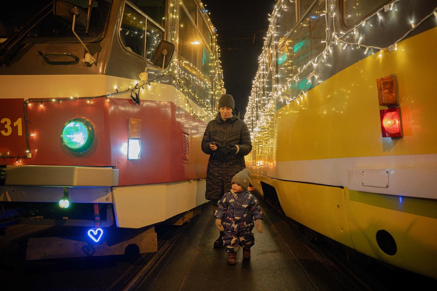 Una donna con un bambino cammina tra i tram decorati con ghirlande il giorno di Natale a Charkiv, il 25 dicembre 2025, durante l'invasione russa dell'Ucraina. (Foto di Ivan SAMOILOV / AFP) (AFP)