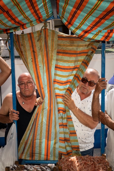 Due persone assistono all’asta del mercato ittico nel porto di Mazara del Vallo. Mazara del Vallo, Sicilia, 2025