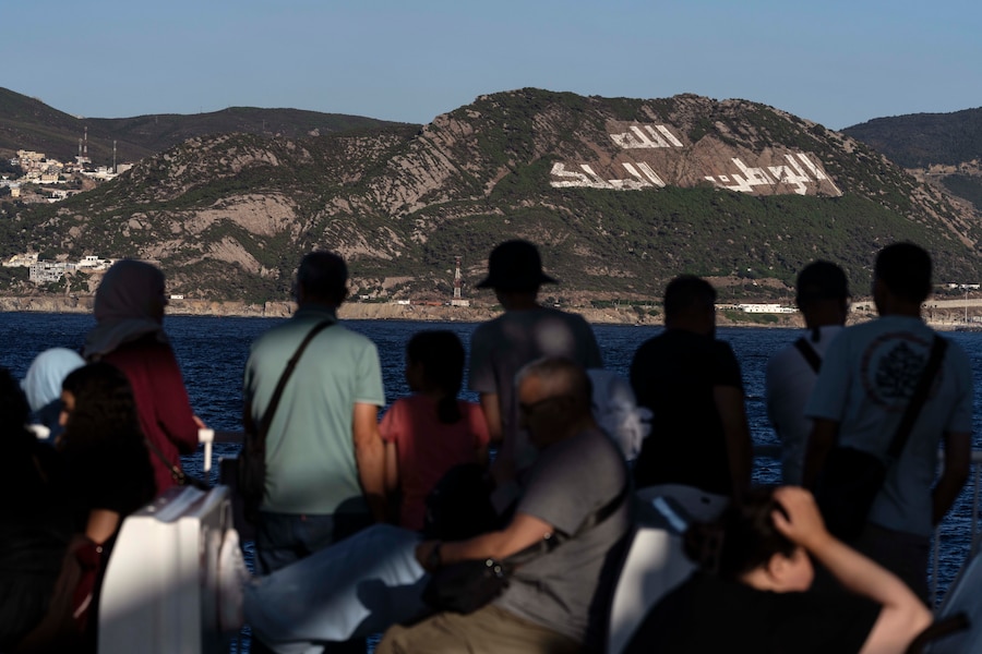 Un gruppo di passeggeri sul traghetto da Algeciras a Tangeri. Sullo sfondo, il motto del Marocco: “Dio, Nazione e Re”. Tangeri, Marocco, 2025