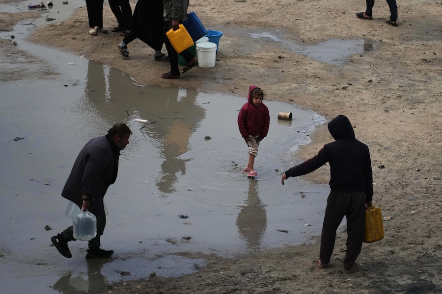 I palestinesi trasportano taniche di plastica piene d'acqua in mezzo al maltempo in un campo profughi nella città di Gaza. (AP Photo/Jehad Alshrafi) (APN)