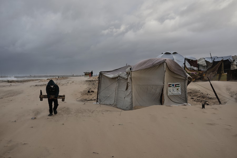 Un uomo trasporta un pezzo di legno in un campo profughi che ospita palestinesi su una spiaggia durante una tempesta a Gaza City. (AP Photo/Jehad Alshrafi) (APN)