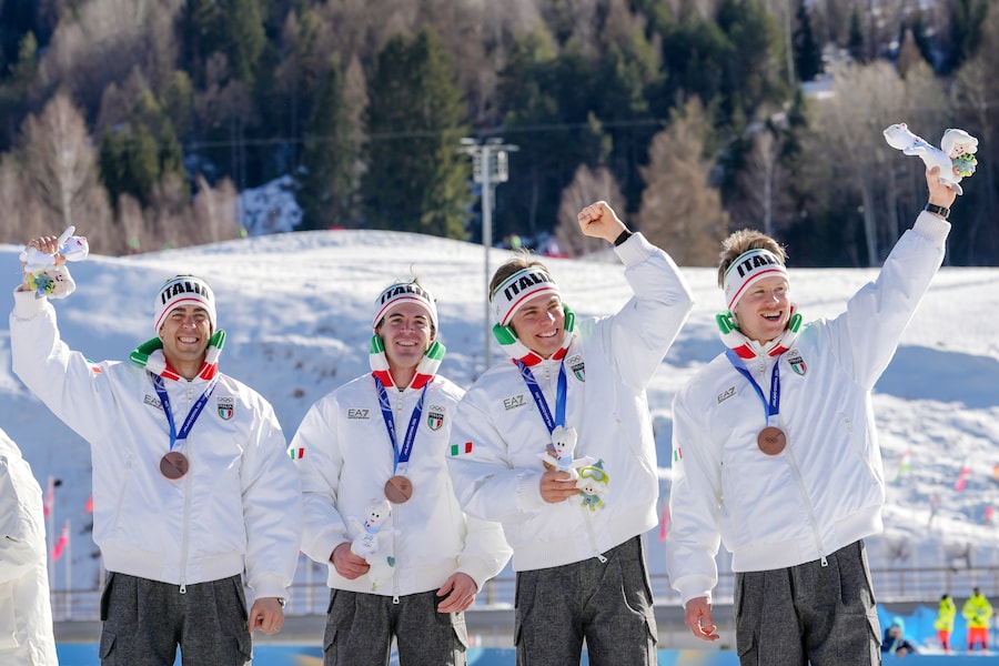 Davide Graz, Elia Barp, Martino Carollo e Federico Pellegrino, dell'Italia, salutano dal podio dopo aver vinto la medaglia di bronzo nella staffetta 4 x 7,5 km maschile di sci di fondo alle Olimpiadi invernali del 2026, a Tesero, Italia, domenica 15 febbraio 2026. (AP Photo/Kirsty Wigglesworth/APS)