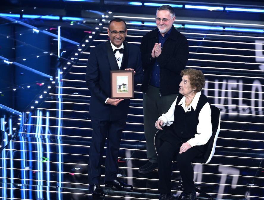 Il conduttore e direttore artistico del Festival di Sanremo Carlo Conti (a sinistra) con la signora Gianna Pratesi (a destra), italiana di 105 anni, e suo figlio (al centro) sul palco del Teatro Ariston durante la 76ª edizione del Festival della Canzone Italiana di Sanremo, Sanremo, Italia, 24 febbraio 2026. (ANSA/Ettore Ferrari)